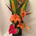 An arrangement of tropical flowers in a black vase.