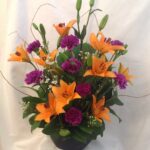 An arrangement of orange and purple flowers in a black vase.