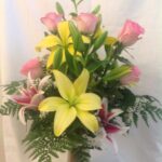 A vase with pink and yellow roses and lilies.