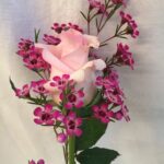 A pink rose in a vase with pink flowers.