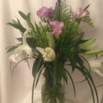 A vase filled with purple flowers and white lilies.